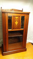 Front view of antique music cabinet showing wood finish, beveled mirrors, and carved top.