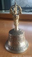 Front view of the Tibetan Buddhist brass bell showing the ornate handle and decorative embossed body.
