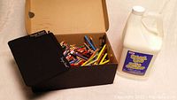 Used boogie board with black carrying pouch, box of colored pencils, and large white jug of school glue