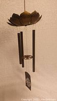 Wind chime showing brass lotus flower top with three black tubes and hanging shou symbol plate