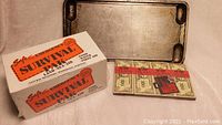 Photo of the used Coleman griddle, unopened survival kit box, and cash-like vintage firestarters.