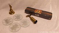 Overview photo showing brass bell shaped like Statue of Liberty, 4 round glass coasters with Indigenous art, solid brass corkscrew, and sealed mini glass mugs box.
