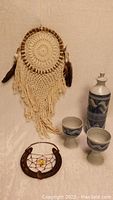 Photo showing large macrame dreamcatcher with feathers, rustic horseshoe dreamcatcher, and ceramic drinkware set with decanter and two cups.