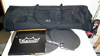 Black nylon drum gear storage bag, drumhead folder with Remo logo, two rubber drum mute pads and chrome drum clamp hardware on tabletop