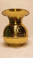 Front view of shiny goldtone metal chewing spittoon with embossed logo and text