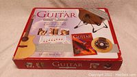 Red box of complete guitar instructional kit showing front with guitar, DVD, book and stand images
