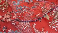 Close-up of intricate Asian design on red silk fabric showing trees, flowers, and pavilion details.