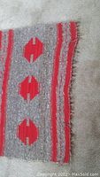 Close-up photo of the rug showing red geometric shapes and striped pattern with frayed edge detail.