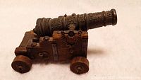 Front side view of the vintage Spanish replica brass cannon mounted on a wooden carriage with wheels and chain details.