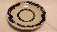 Top-down view of the round serving plate showing cobalt blue wavy decoration along edges and concentric circles in center on beige background.