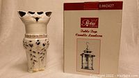 Porcelain cat candle holder next to boxed brass candle lantern.