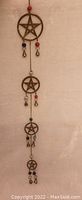Full view of vintage solid brass pentacle hanging art with four connected pentacles, colorful beads, and small bells.