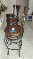 Three brown vinyl padded high counter stools aligned next to a kitchen counter. Visible scratches and wear on seats and frames.