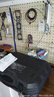 Wide view of the black Craftsman cutting tool case on a surface with various tools hanging on the pegboard behind it.