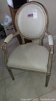 Front view of one beige upholstered oval-back armchair with carved and distressed ash-white wood frame