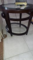 Full side view of oval 2-tier end table showing espresso wood frame, glass top and bottom shelf, and floor tiles beneath.