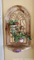 Frontal view of weathered outdoor wall art with rustic arched wooden frame, metal decoration, two faux ivy potted plants attached