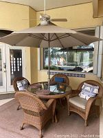 Full view of round wicker table with beveled glass top, umbrella inserted, placemats on glass surface, surrounding chairs