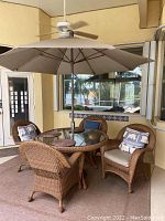 Set of two outdoor wicker chairs with cushions and throw pillows around a glass table and umbrella