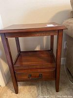 Full front view of wooden end table showing drawer with black metal handle and lower shelf.