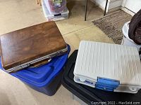 Shows plastic tubs with a brown briefcase and white briefcase stacked on top