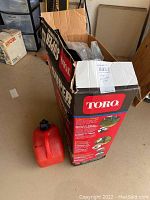Photo of open Toro branded box and red gas canister on floor