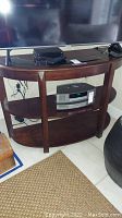 Full front view of curved wood TV stand with electronic devices on and around it.
