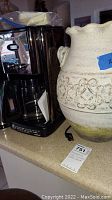 Side view of coffee machine next to decorative urn on countertop showing size and condition.