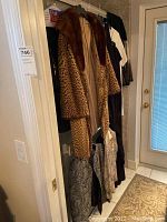 Photo showing multiple garments on hangers including a brown faux fur leopard print coat, a black dress, and more hung on a rack near a door.