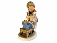 Front and side view of the Hummel figurine showing the young girl stirring in a blue pot on a wooden stool on a circular base.