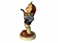 Side profile showing the figurine of a young boy in hiking outfit, detailed painting, holding a walking stick and small bag, standing on a round base.