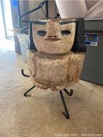 Front view of the carved heavy sculpture showing the face and body on metal stand