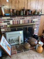 Wide shot showing multiple South American pottery items on fireplace mantel and hearth, with two framed art prints leaning against fireplace.