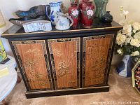 Front view of lacquered wood buffet cabinet, showing three decorative doors with gold and wood designs, and various items on top (not included).
