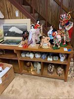 Wide view showing shelf with multiple Asian themed figures, ceramic vases, framed photos, and decorative art pieces.