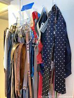 Belts and suspenders hanging on a rack showing various materials and colors including leather, fabric, and patterned designs.