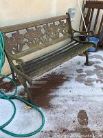 Full view of the metal and wood outdoor garden bench with floral design backrest, showing rust and wear.