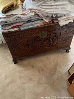 Full view photo of the carved wood chest with fabrics stacked on top