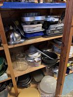 First photo shows wooden shelving with stacked and organized cookware and serving wares including metal pans, cake plates, glass jars, bowls, and assorted kitchenware.