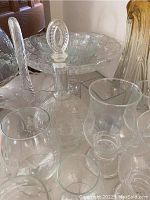 Clear glassware including cake plate with dome, decanters, and various glasses, displayed on table