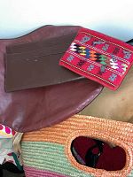 Photo showing brown leather handbag, red multi-color embroidered fabric bag, and woven insulated bag with round handle cutouts.