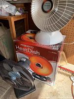 Presto HeatDish electric heater with its original box and Holmes electric fan placed on top and beside the box.