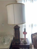 Wide view showing two lamps: taller wood carved table lamp with white shade on left and smaller pink glass table lamp with brass base on right on wood side table