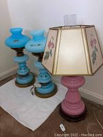 Photo of two matching blue glass lamps and one pink base lamp with floral shade showing overall condition and design.