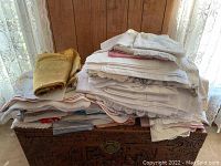 Large pile of folded linens including yellow, white, and striped pieces on top of a wooden chest