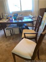 Rectangular dining table with various objects on top, surrounded by chairs.