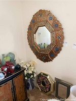 Large Asian inspired wall mirror with scalloped edges and intricate gold floral pattern with touches of blue and white on a red background, hung on wall above furniture.