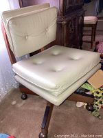 Full view of mid century modern office chair showing beige cushioned seat and back with button tufting, wood frame and wheels at base.