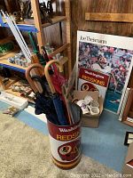 Photo showing Washington Redskins umbrella stand filled with umbrellas, next to posters and a box of mugs.
