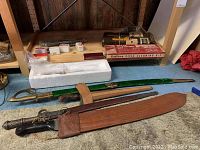 Variety of swords, blades, cleaning kit and pellet tins on shelf